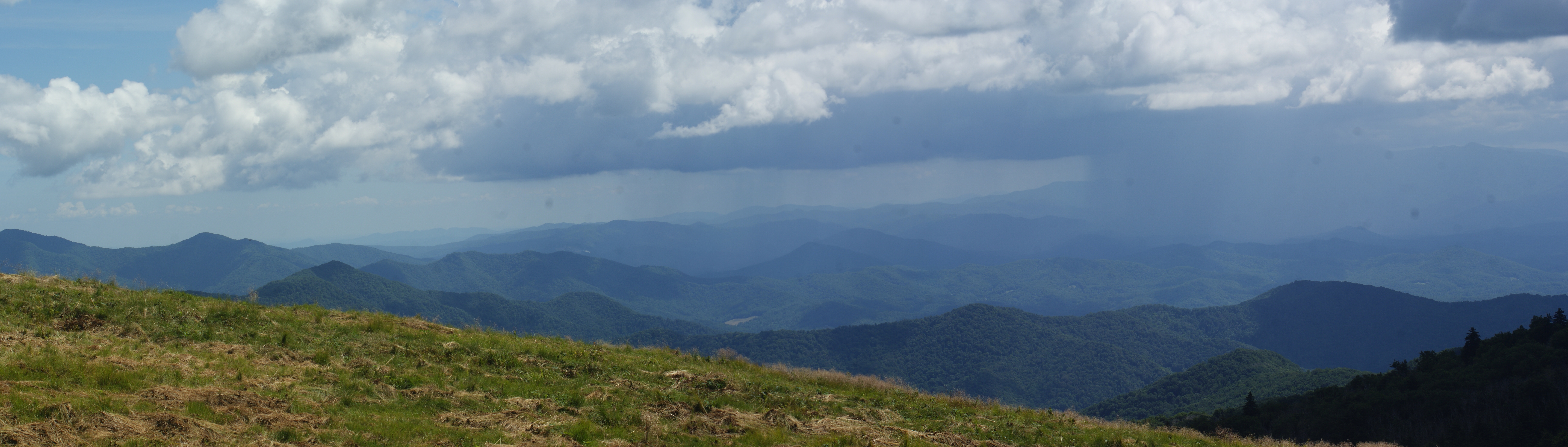 Panoramic view of Roan Mountain in western North Carolina with dark storm rain clouds gathering over the rolling green forested ridges, illustrating the heavy rainfall conditions that trigger landslides